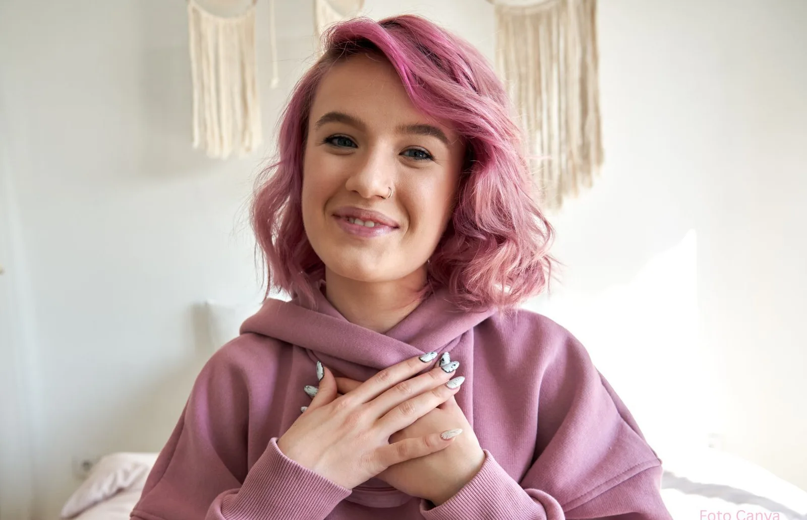 Teenagerin mit rosa Haaren und lila Hoodie lächelt dankbar und entspannt, Hände vor der Brust