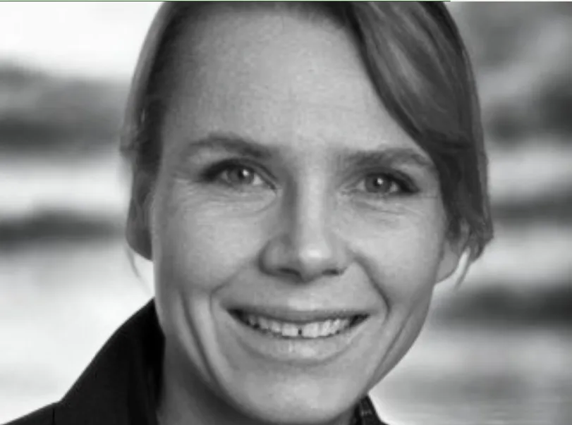 Schwarz-Weiß-Porträtfoto von Jessica Meyer Rachner, brünette Haare, freundlich lächelnd vor Meer