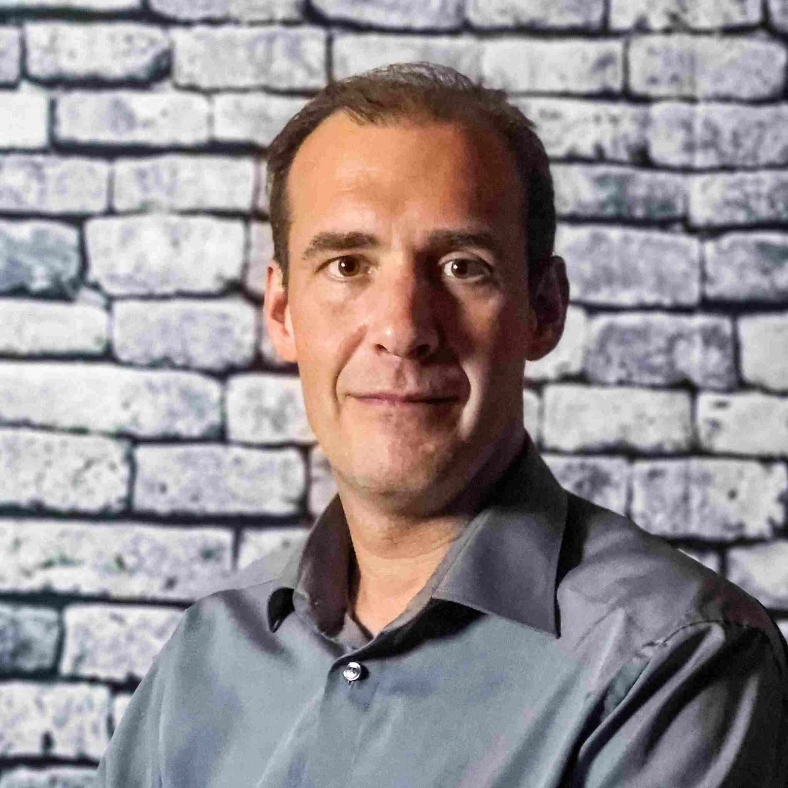Portrait eines Mannes mittleren Alters mit dunklem Hemd vor grauer Backsteinmauer