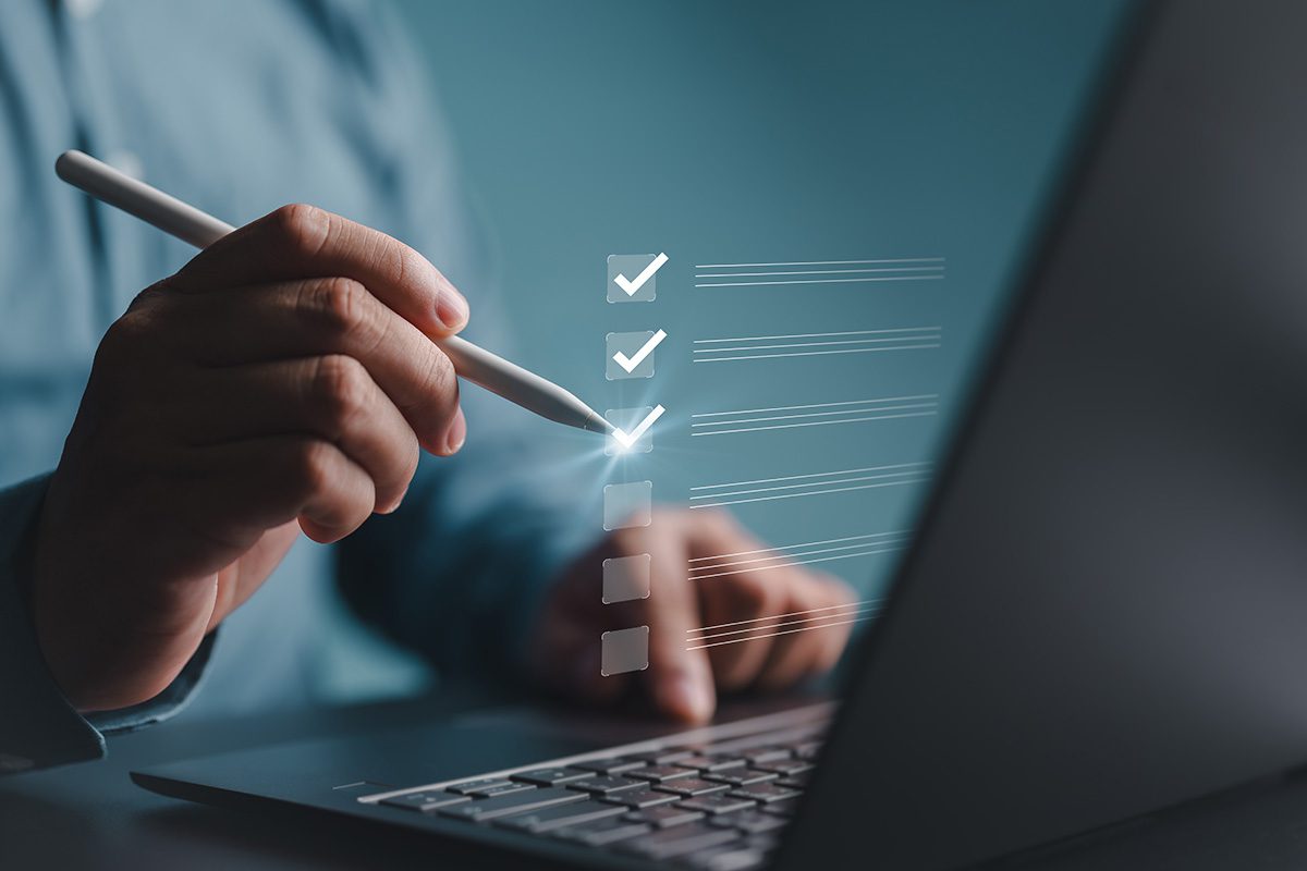 Hand mit Stift zeigt auf holografische Checkliste mit Häkchen auf Laptop-Bildschirm