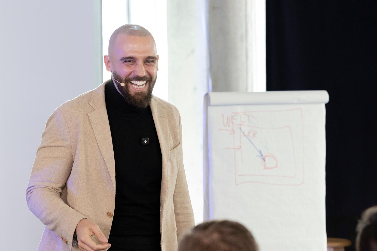 Athanasios Nasopoulos in Beige-Blazer lachend vor Flipchart im Seminar