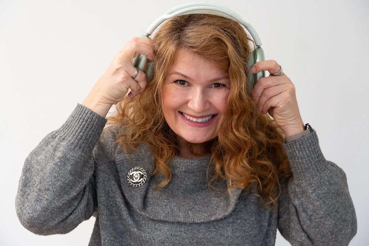Eva Möller mit hellgrünen Kopfhörern, lachend, graues Sweatshirt, weißer Hintergrund