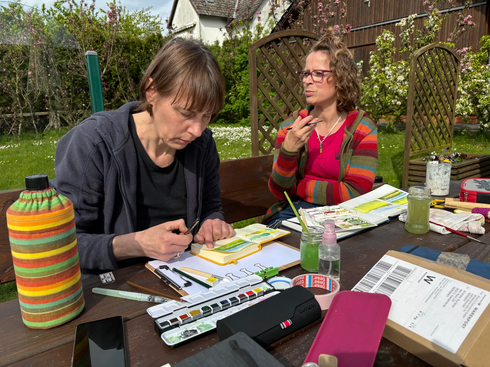 Art Journaling-Kurse – Videokurse zum Kreativjournal 13 Andrea Gunkler beim Art Journaling mit einer anderen Person im Garten, Materialen und Skizzen auf Tisch