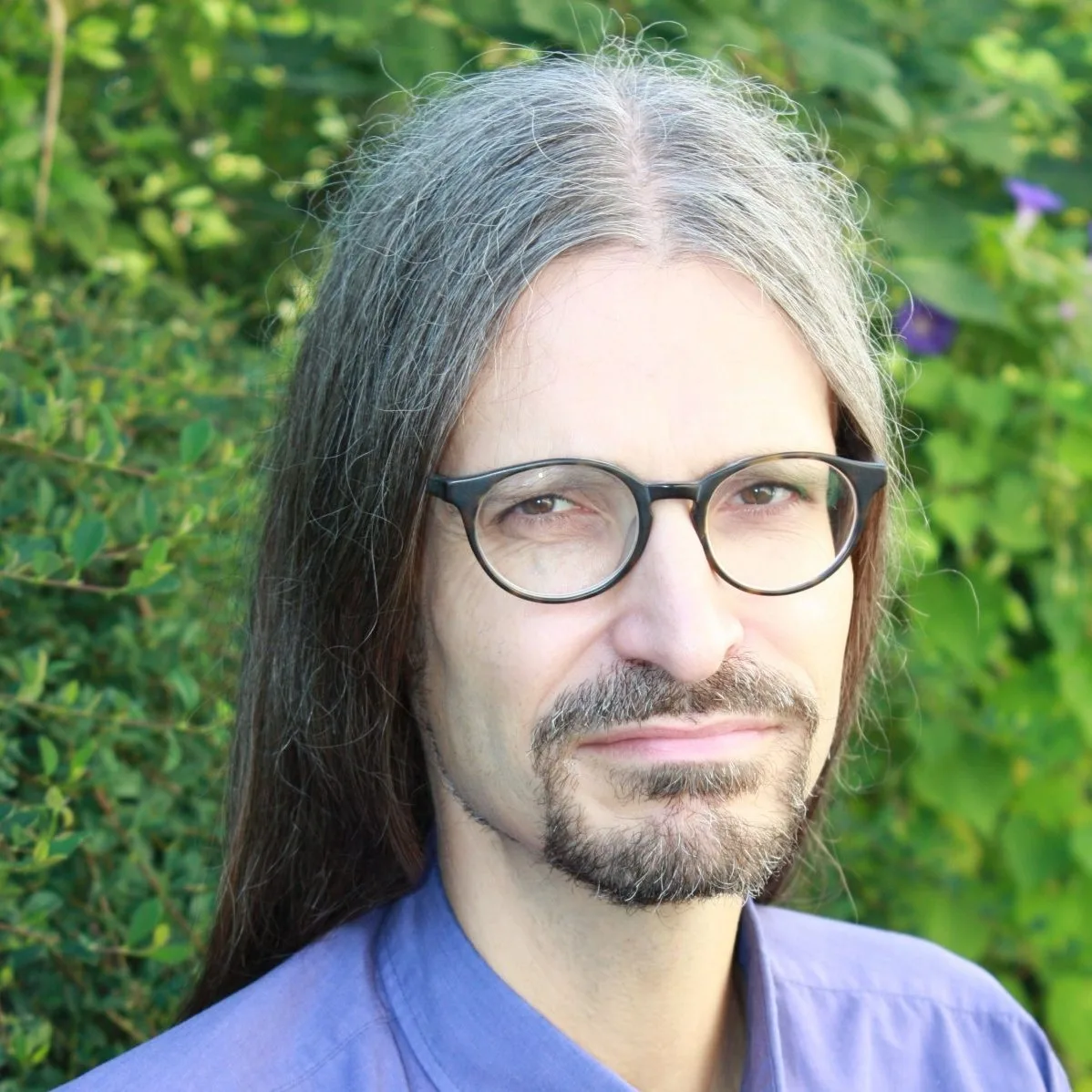 Porträt eines Mannes mit grauem Haar, Brille und Bart vor grünem Hintergrund