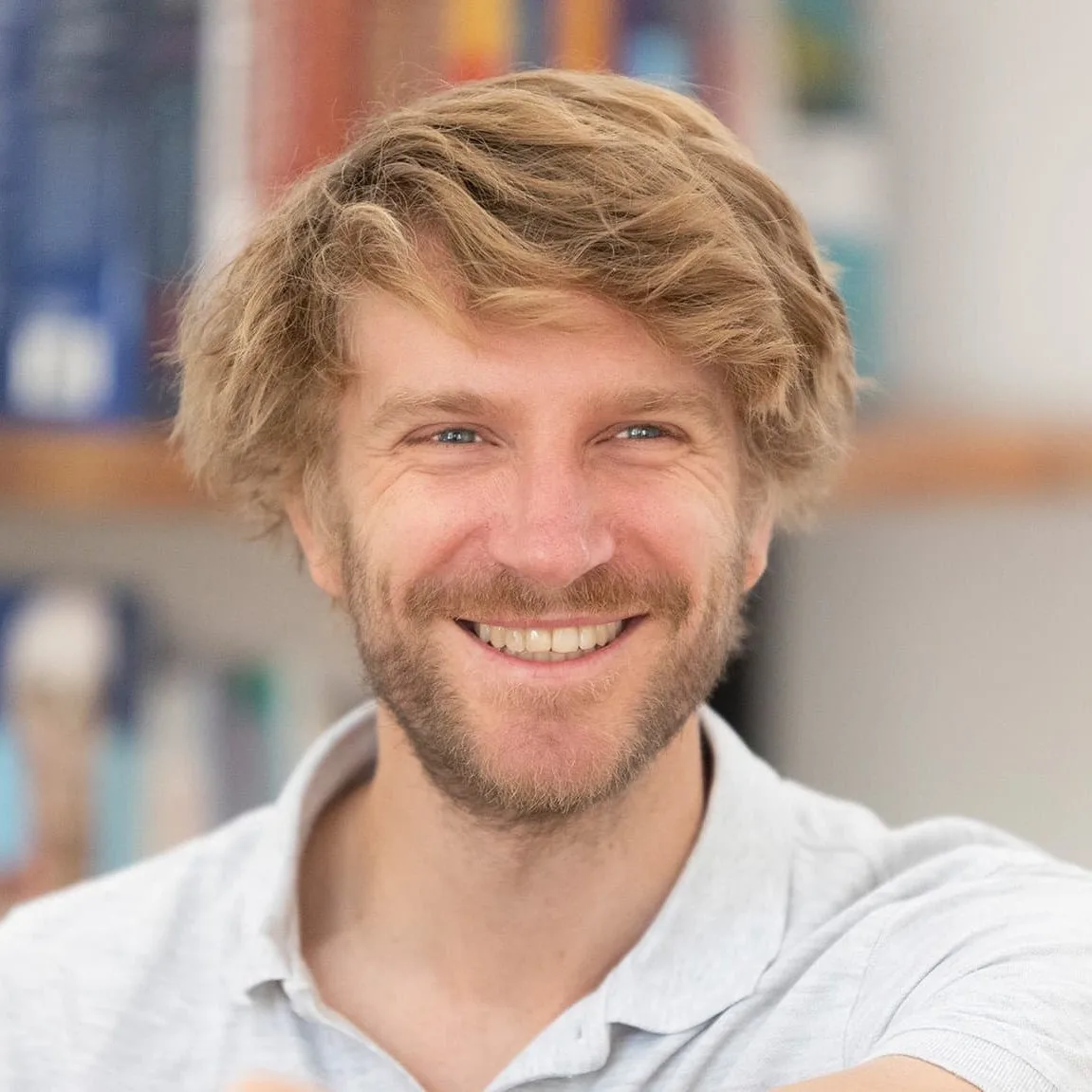 Porträt eines jungen Mannes mit blondem Haar und freundlichem Lächeln in weißem Shirt