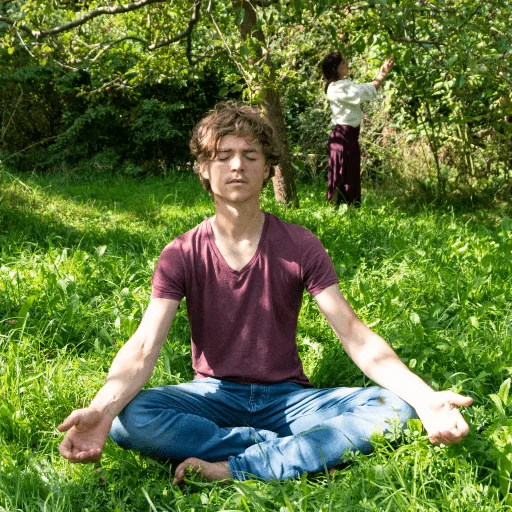 Atemreise – Breathwork-Videokurs 2 Mann in lila Shirt sitzt meditierend auf grüner Wiese in Lotusposition, Fotoshooting 2021