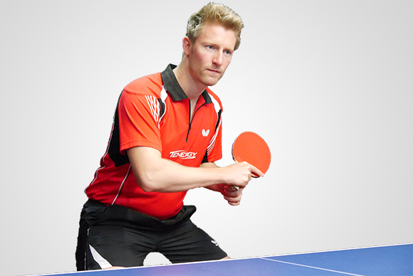 Tischtennisspieler Ruwen in roter Sportkleidung hält Tischtennisschläger und Tischtennisball