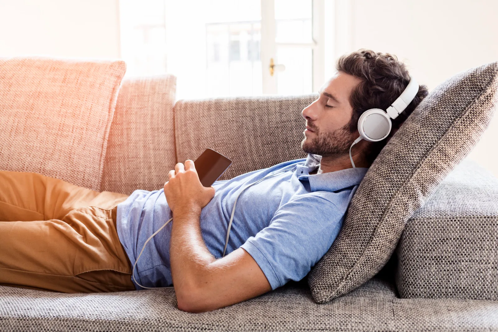 Mann auf Sofa mit Kopfhörern und Smartphone, entspannt zurücklehnt