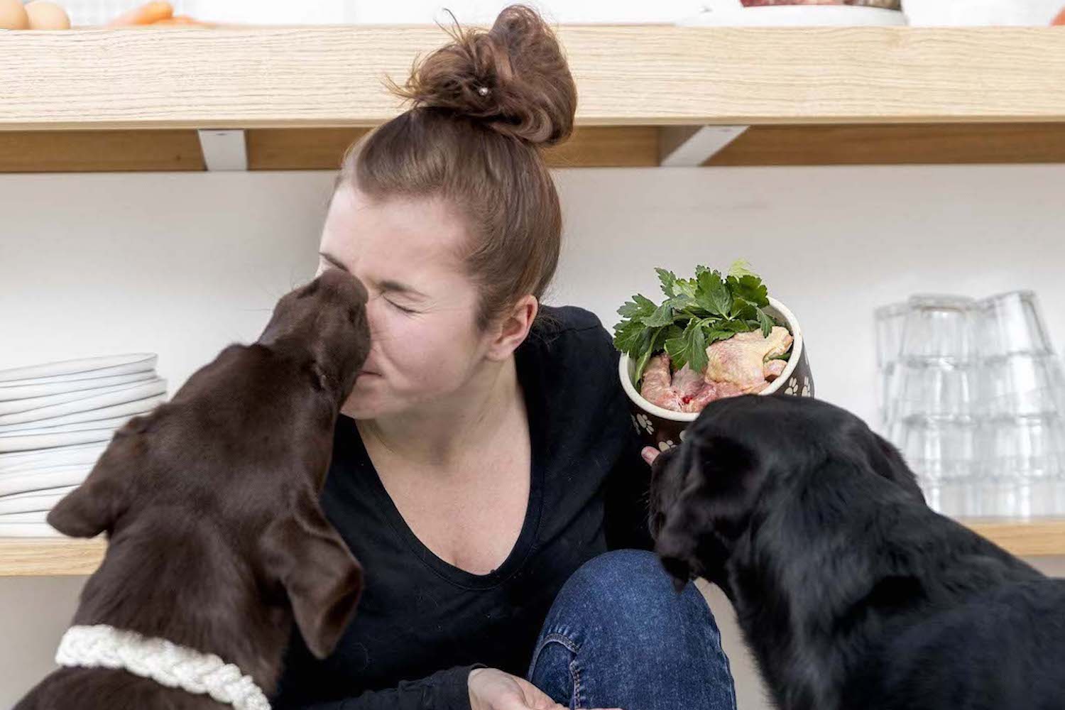 Ausbildung zum Hundeernährungsberater von Paulina Adamczyk 11 Frau mit zwei schwarzen Hunden in moderner Küche mit Napf und Kräutern