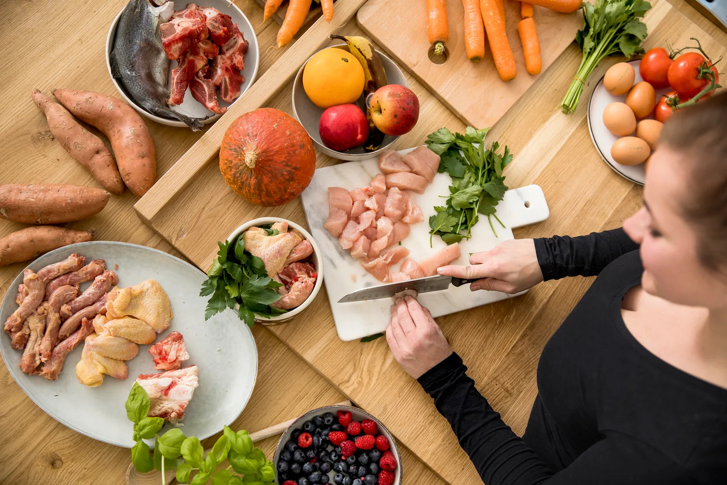 Ausbildung zum Hundeernährungsberater von Paulina Adamczyk 7 Frau schneidet Fleisch auf Holzschneidebrett mit Gemüse und Obst arrangiert