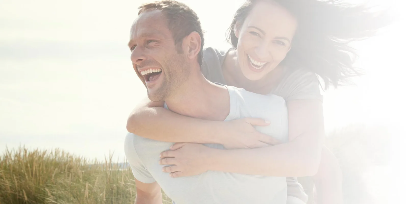 Mann und Frau umarmen sich lachend in sonniger Wiese, Lifestyle