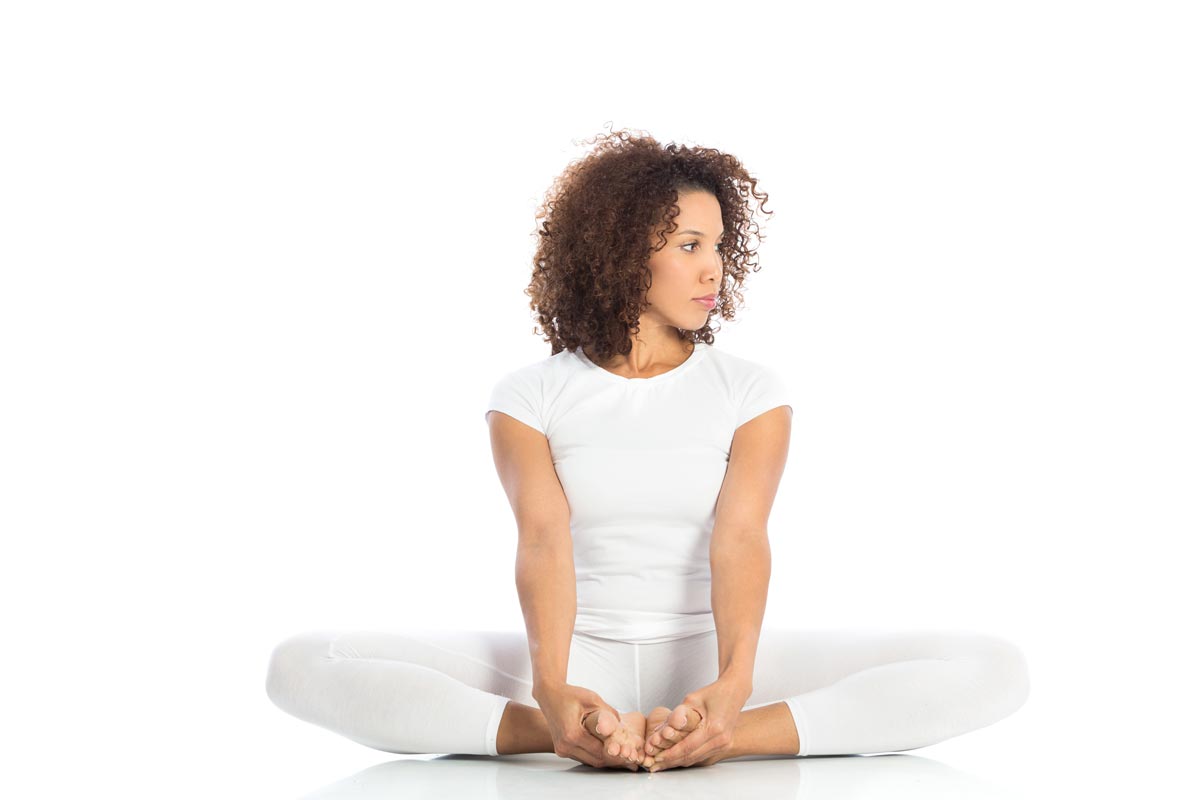 Frau mit braunem lockigem Haar in Lotus-Position, weiße Yoga-Kleidung