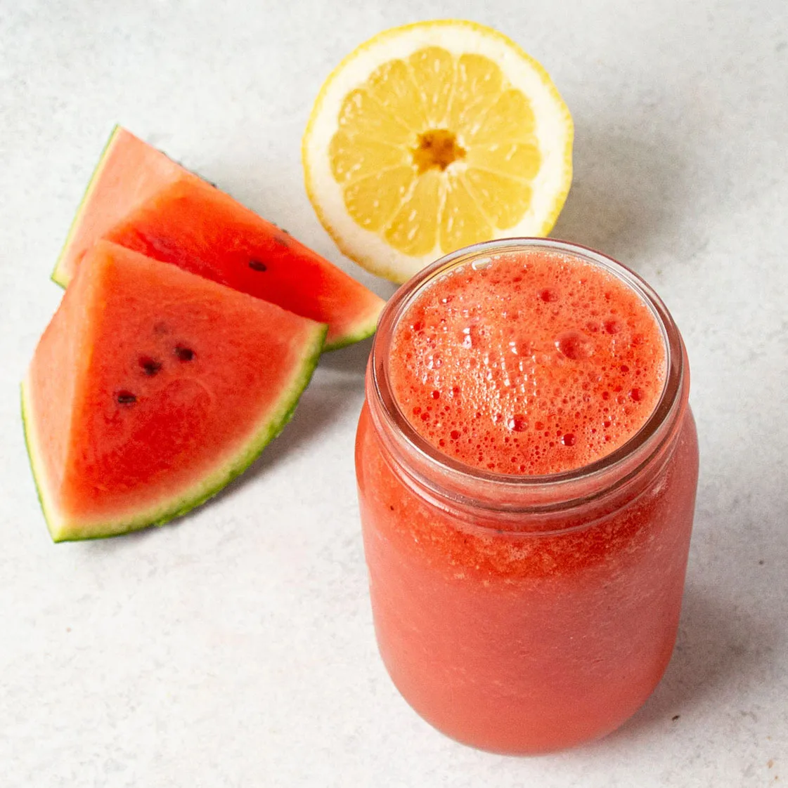 Wassermelonensmoothie in Glas mit Wassermelonenscheibe und Zitronenhälfte