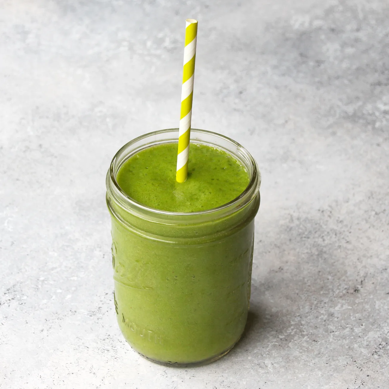 Grüner Matcha Smoothie im Glas mit gelb-weißem Strohhalm