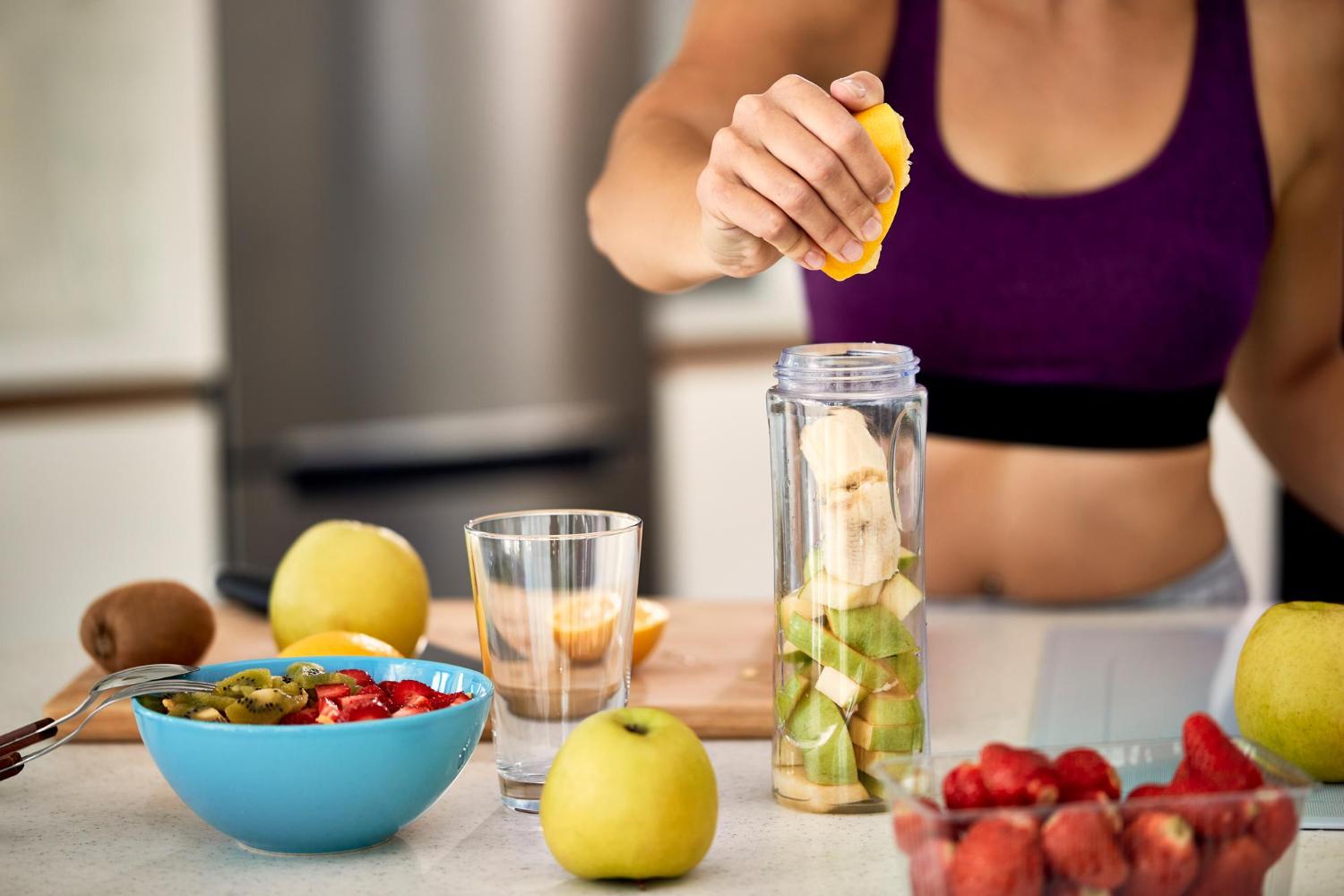 Ayurveda-Kochkurs und Ayurveda-Basics von Wolfgang Neutzler 3 Sportlerin presst Zitrone über Wasser mit Früchten und Gemüse auf dem Tisch
