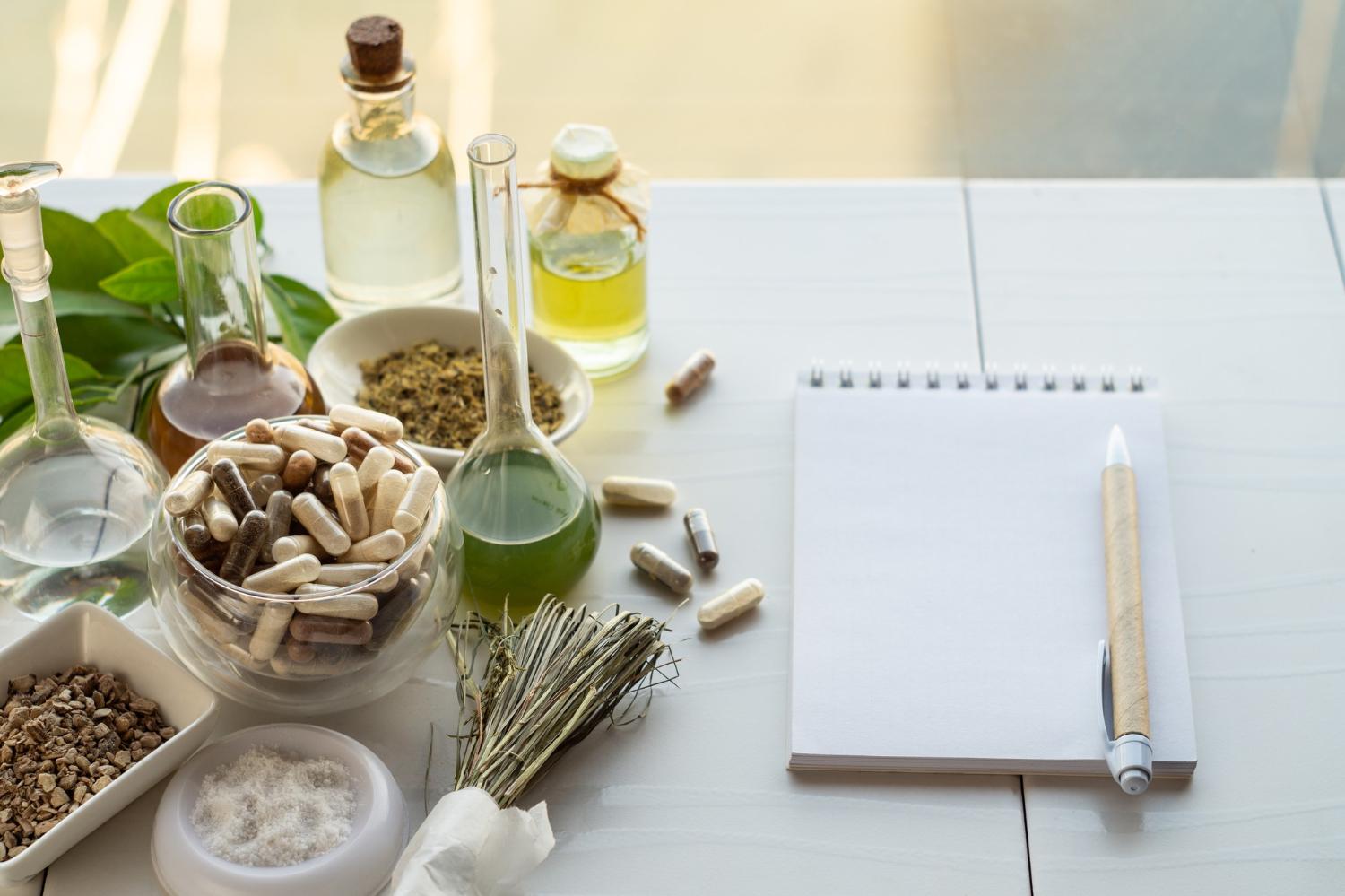 Ayurveda-Kochkurs und Ayurveda-Basics von Wolfgang Neutzler 5 Ayurveda Basics - Heilkräuter, Kapseln, Öle und Notizbuch auf weißem Tisch