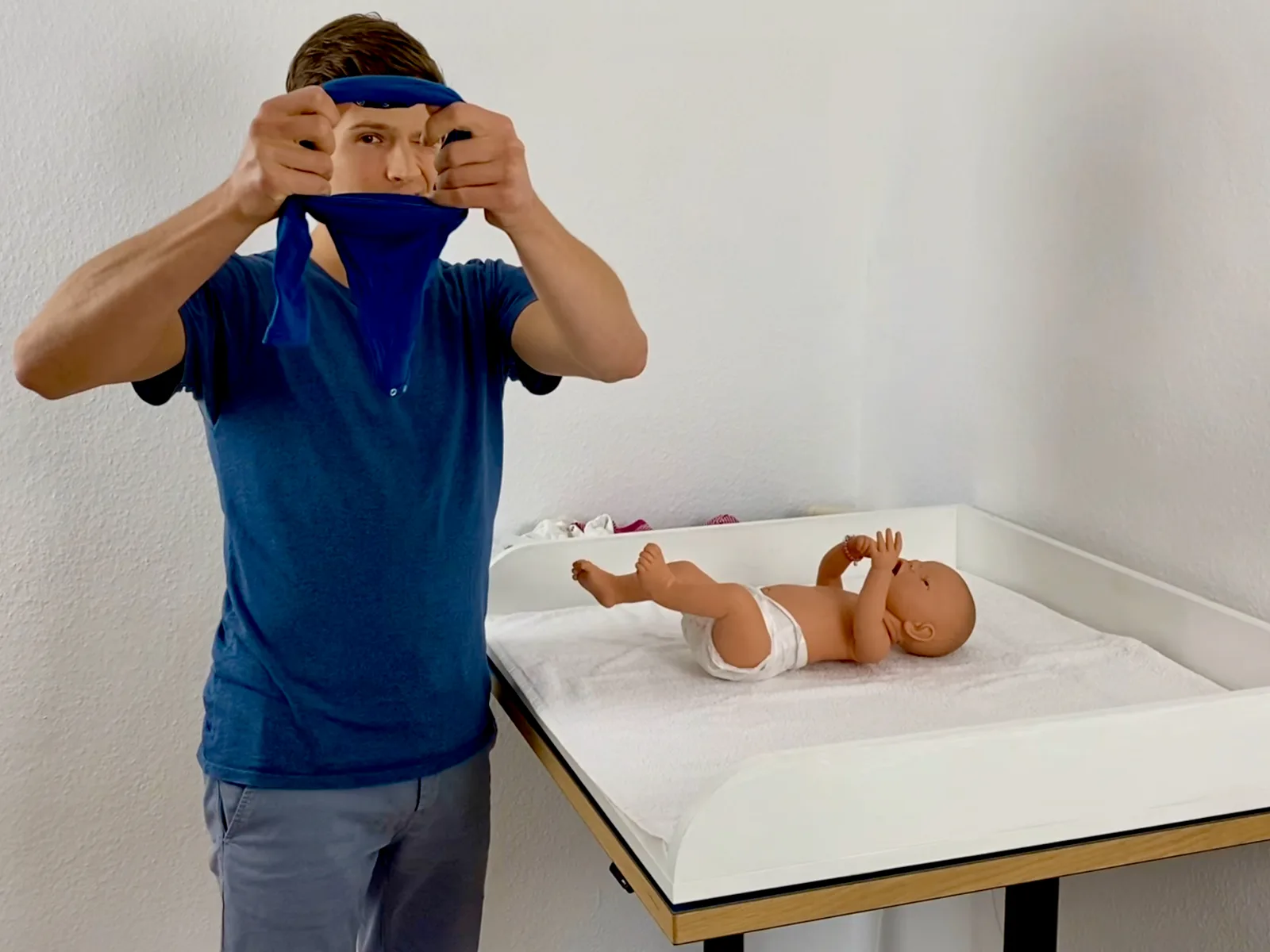Babyhandling – Videokurs für Eltern von Pelle Wiedling 1 Junge mit blauem Stirnband hält Puppe vor Gesicht auf Wickeltisch