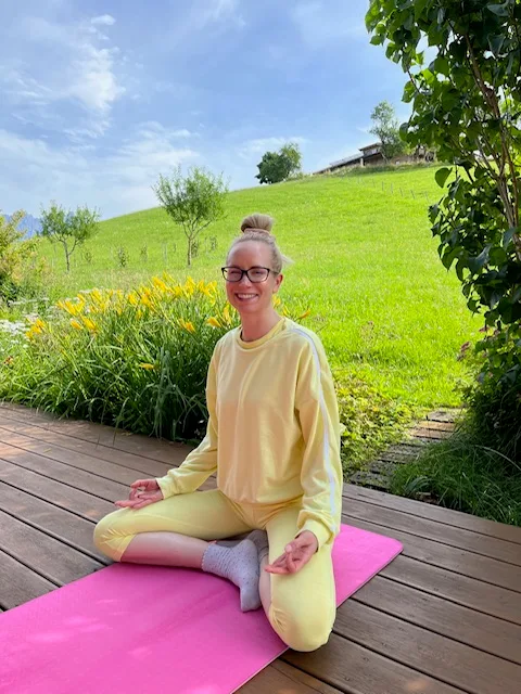 Frau (Justyna) in gelbem Sweatshirt auf rosa Yoga-Matte vor grüner Wiese knietend