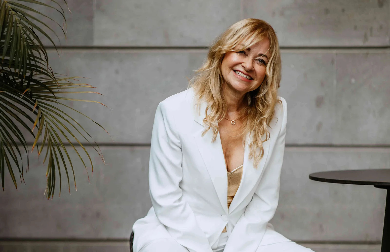 Porträt von Claudia Homberg im weißen Blazer, lächelnd vor grauer Wand