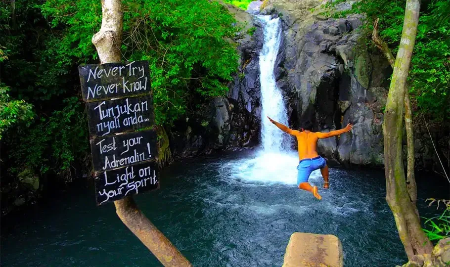 Person beim Handstand unter Wasserfall im grünen Dschungel