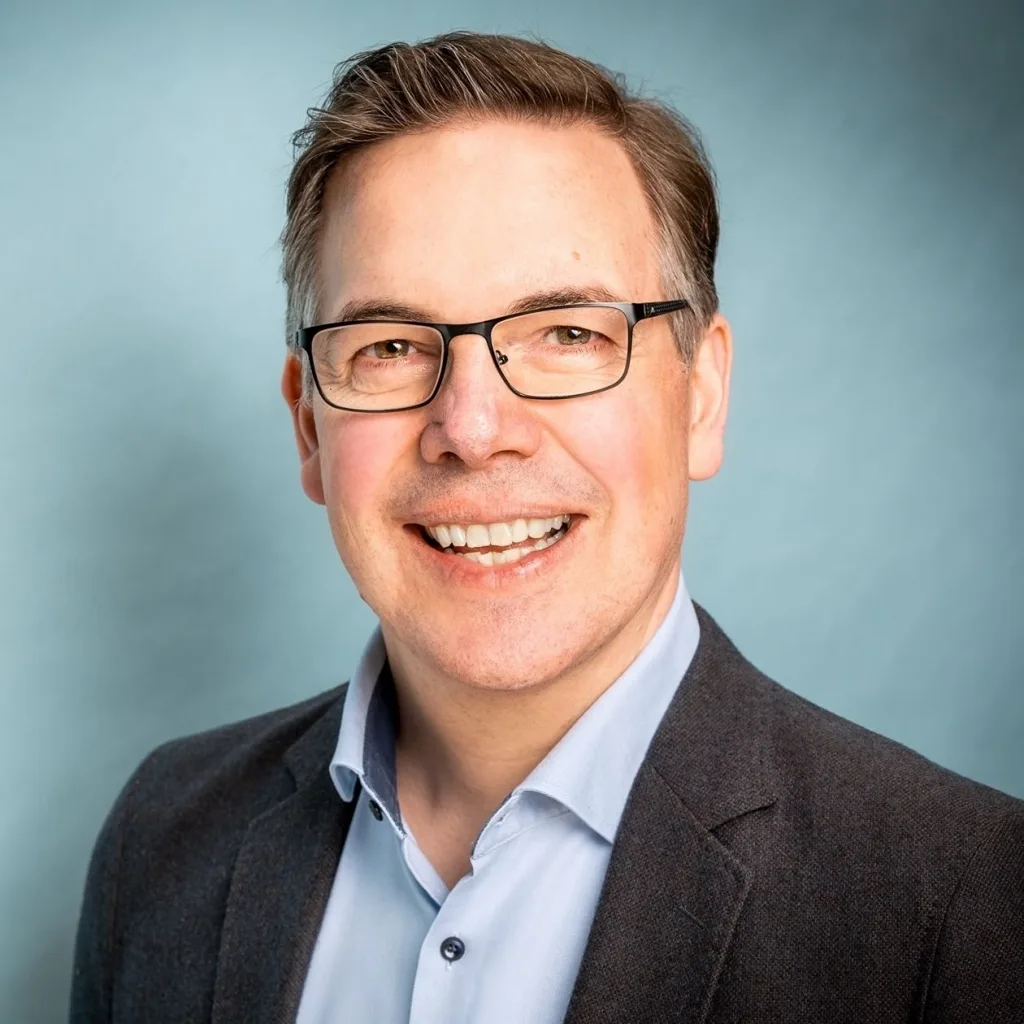 Porträt eines Mannes mittleren Alters mit Brille vor blauem Hintergrund, lächelnd