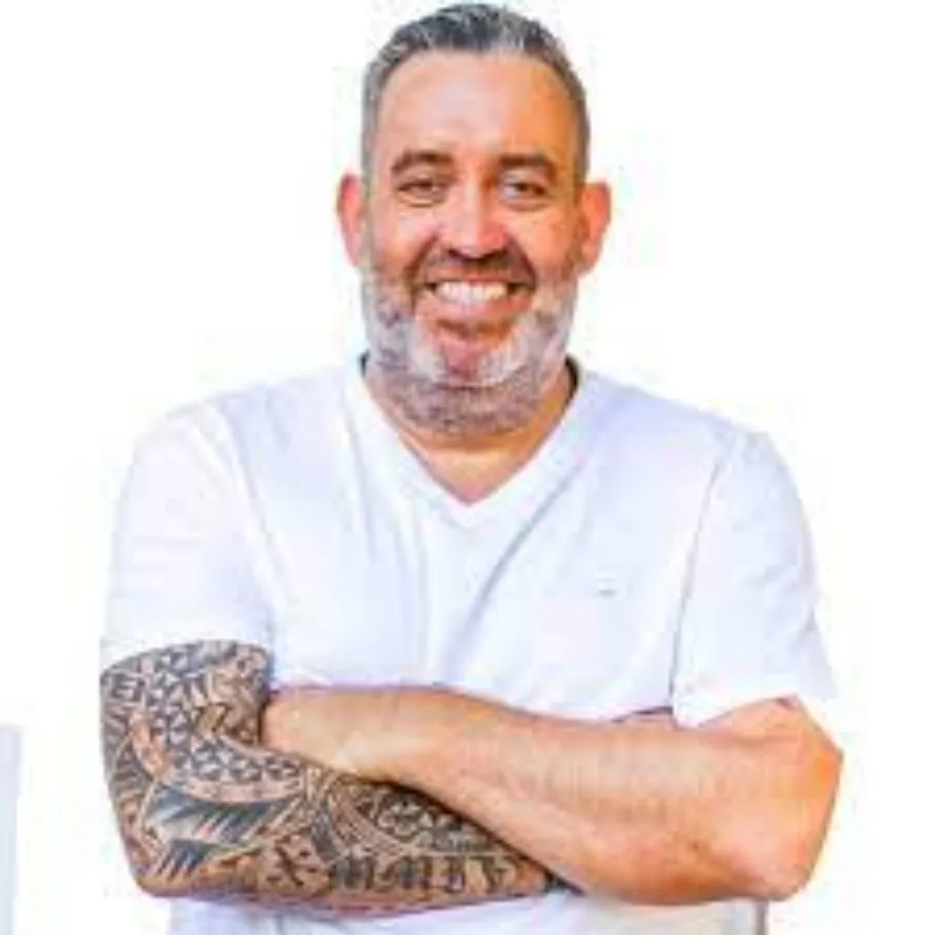 Porträt eines Mannes mit grauem Bart und Tattoo am Arm im weißen T-Shirt