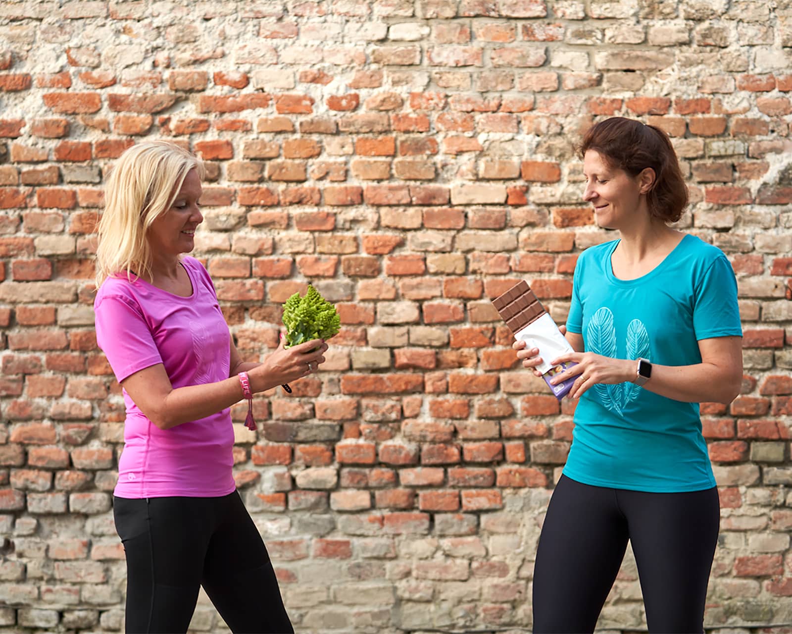 Zwei Frauen vor Backsteinwand mit Salat und Schokolade – Workshop Bauchspeck