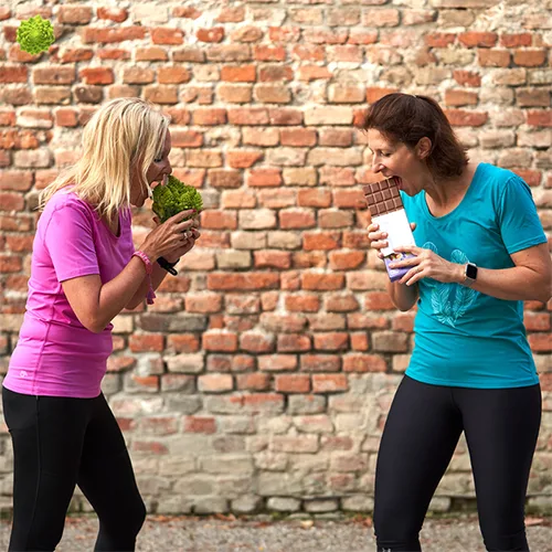 Zwei Frauen vor roter Backsteinwand mit Salat und Schokolade – Workshop