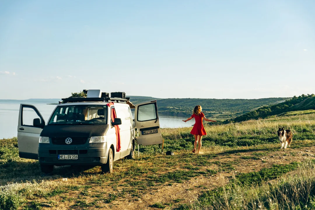 Bauplan Fiat Ducato – Stracciatella Campervan 2 Frau in rotem Kleid mit Hund neben Volkswagen Campervan in Landschaft mit See