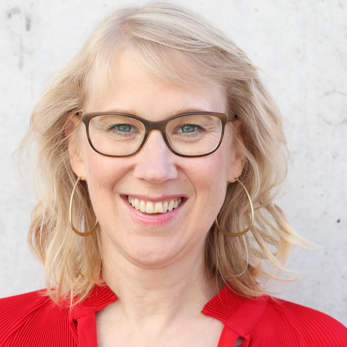 be ORIGINAL – Videokurs zur Positionierung von Monika Frauendorfer 11 Kundenstimme: Frau mit blonder Welle, Brille und Perlenkette vor grauem Hintergrund, strahlendes Lächeln