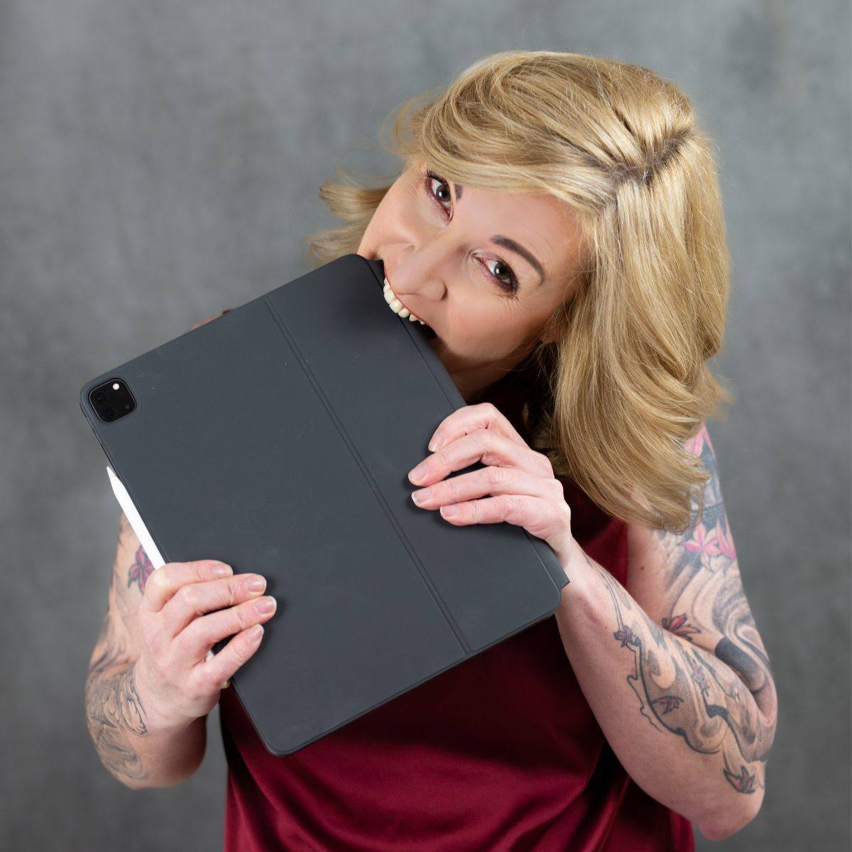 be ORIGINAL – Videokurs zur Positionierung von Monika Frauendorfer 9 Kundenstimme: Blonde Frau mit Brille und Tätowierungen hält schwarzes Tablet lächelnd in die Kamera