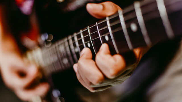 Nahaufnahme von Gitarrenhänden auf Griffbrett beim schnellen Spielen