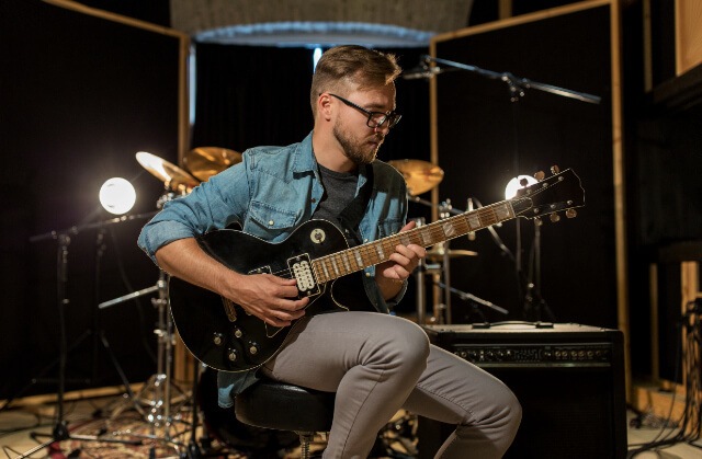 Gitarrist mit Brille spielt schwarze E-Gitarre im professionellen Tonstudio mit Beleuchtung