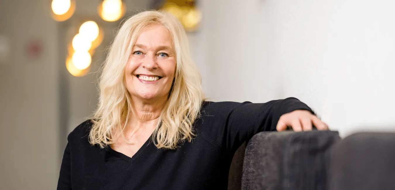 Behind Your Eyes – Audiokurs zur Selbsterkenntnis von Helene Griebe 2 Porträt von Helene Griebe, blonde Frau in schwarzem Oberteil vor warmem Lichthintergrund