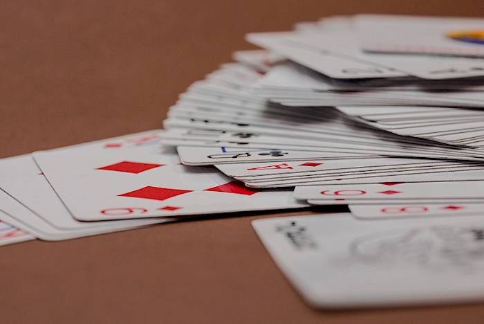Spielkarten mit Karo-Symbolen auf braunem Untergrund, gestapelte Kartenstapel im Hintergrund
