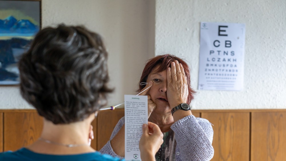 Coaching-Sitzung zwischen zwei Frauen mit Sehtafel im Hintergrund, eine Frau hält ein Testblatt