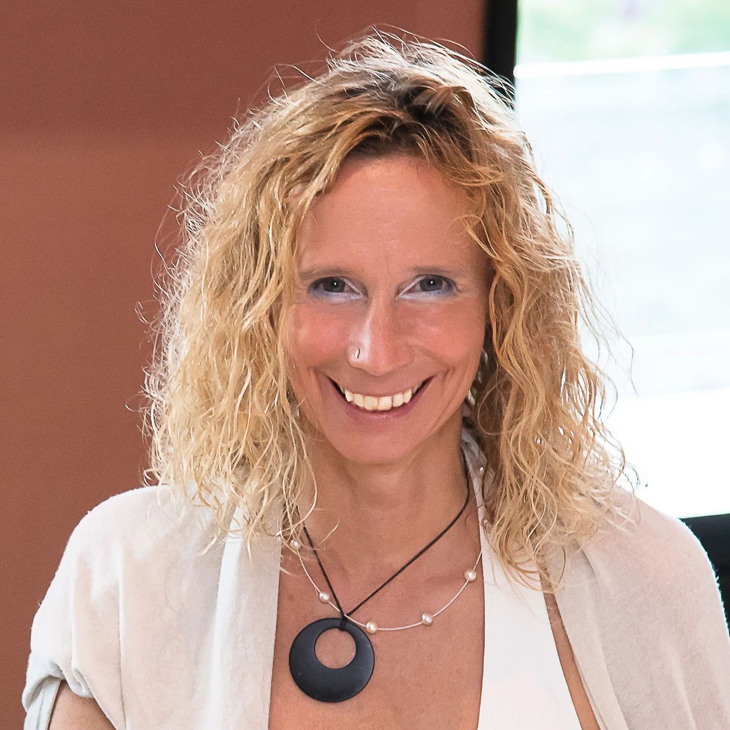 Liv Wach Portrait mit lockigem blonde Haar, weißem Oberteil und schwarzem Anhänger-Halskette
