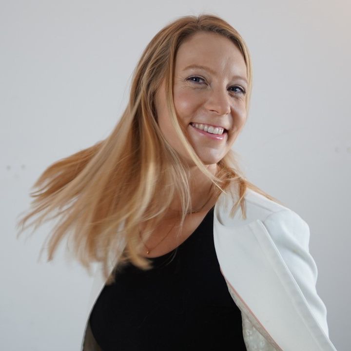 Frau mit rötlich-blondem Haar in schwarzem und weißem Blazer, lächelnd, Haare beweglich