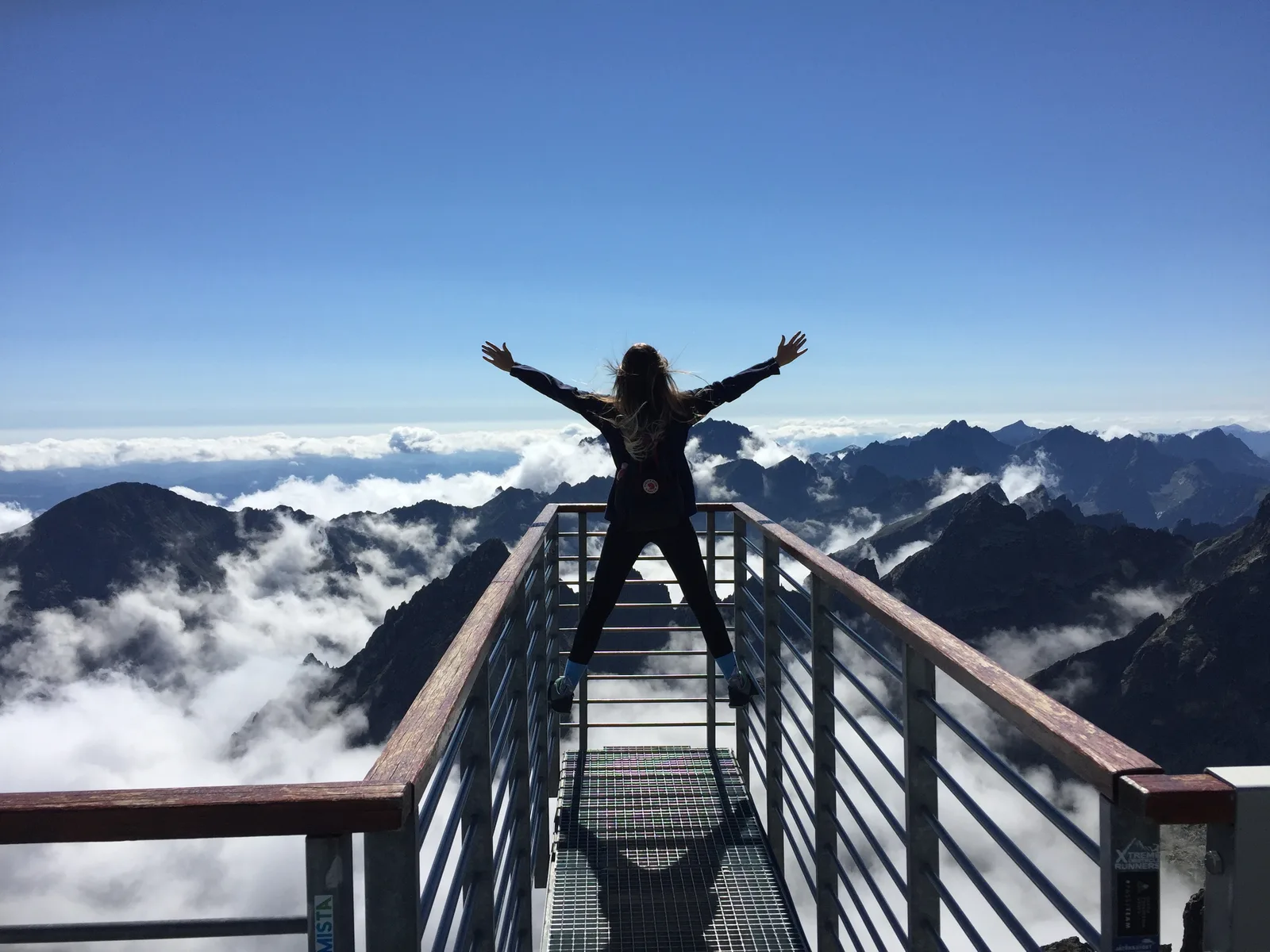 Person mit Armen erhoben auf Bergsteg, Bergketten, Wolken