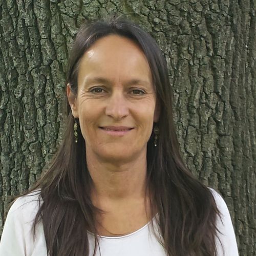 Porträtfoto von Natalie Mackel vor grauer Baumrinde, Frau mit dunklem Haar