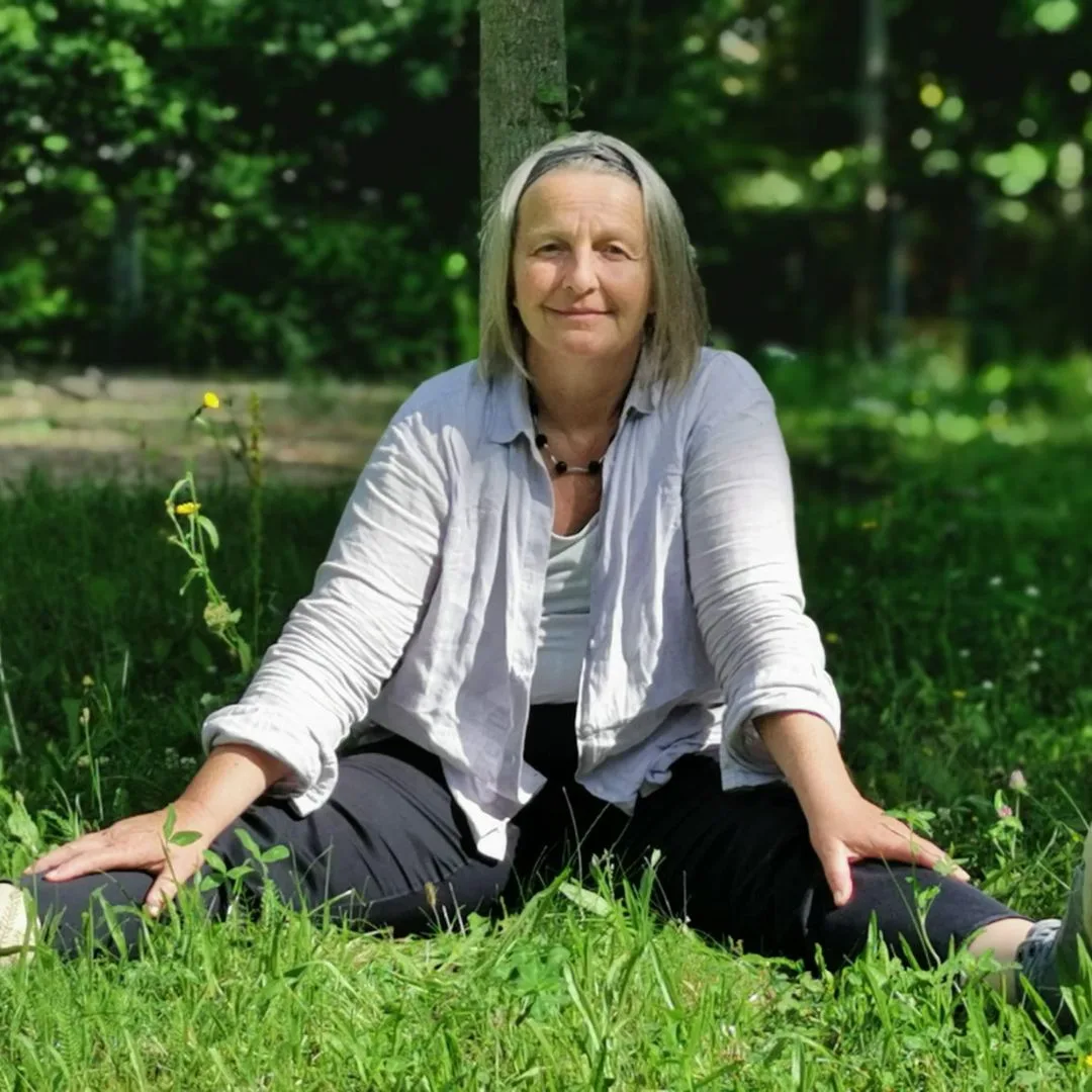 Porträtfoto von Ulrike Röth, Frau mit grauem Haar im Freien auf Gras sitzend
