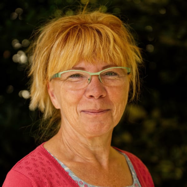 Porträt von Liane Klar, Frau mit rötlich-blondem Haar, grüner Brille und rosa Shirt