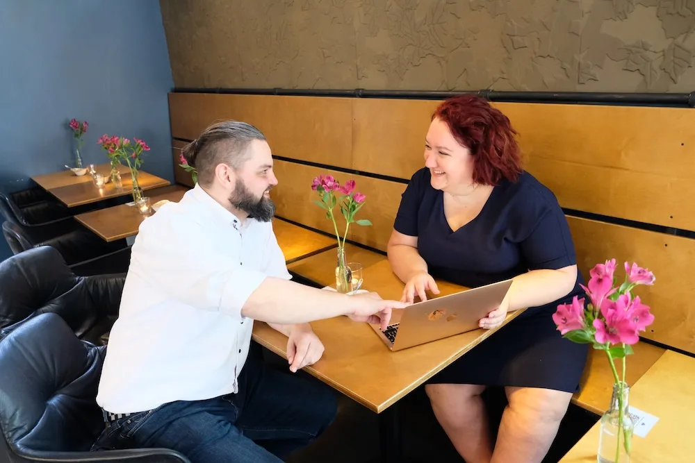 Mann und Frau sitzen sich gegenüber am Tisch, arbeiten zusammen am Laptop