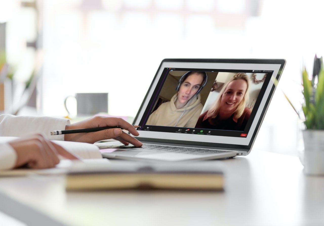 Frau bei Videokonferenz mit zwei Personen auf Laptop-Bildschirm, Schreibtisch mit Notizbuch