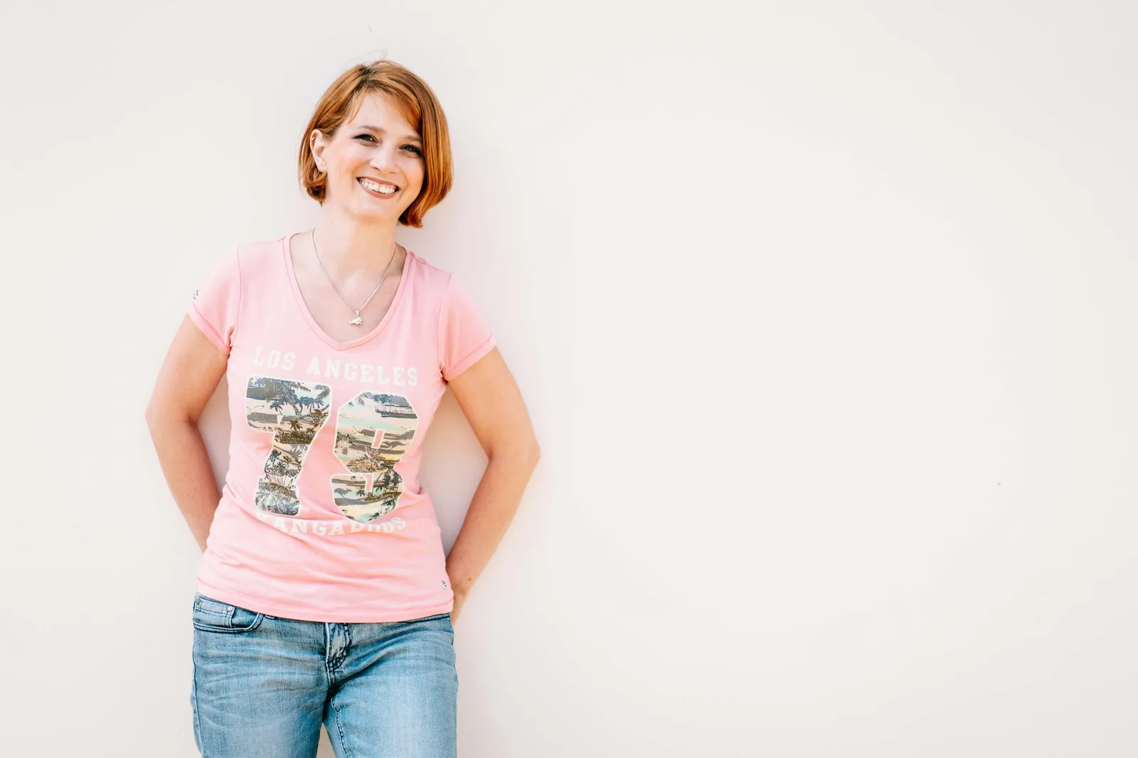 Petra Ecker lächelnd in rosa Top mit Jeans vor weißem Hintergrund