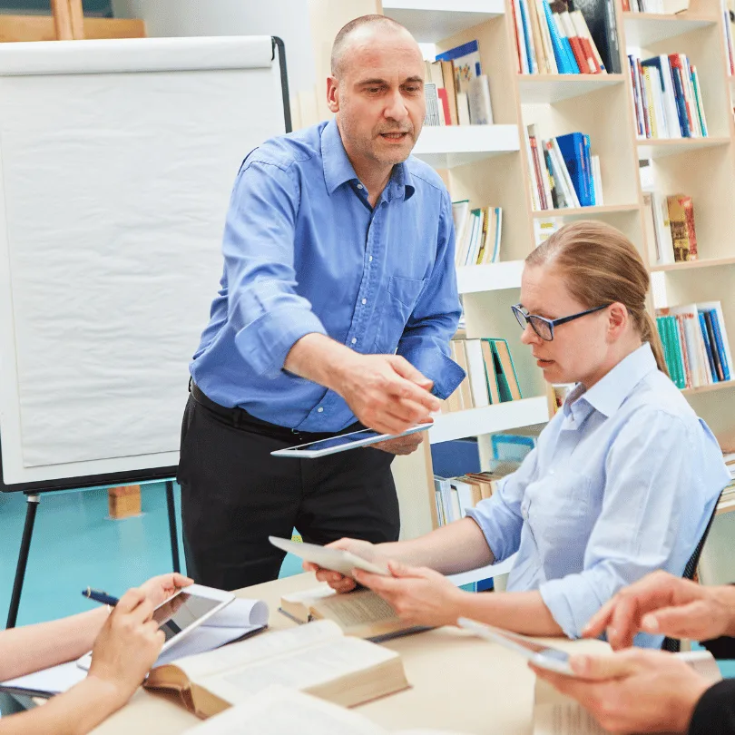 Mann in blauem Hemd erklärt Frau in Büroumgebung mit Flipchart und Bücherregalen, Geschäftsmeeting, 810×810 Pixel