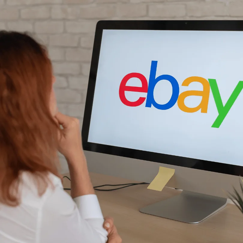 Frau von hinten sitzt vor Monitor mit eBay Logo auf dem Bildschirm, Büroumgebung mit Ziegelhintergrund