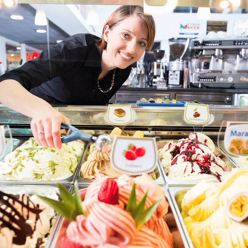 Businessplan Eiscafé – Vorlage mit Excel-Finanzplan von Dirk Leimkuhl 4 Frau in schwarzem Hemd an Eiscafé-Theke mit Eisbecher und Vitrine voller Eissorten