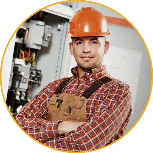 Elektroinstallateur mit rotem Hemd, orange Schutzhelm und Werkzeuggürtel, vor Elektroschaltkasten mit Sicherung