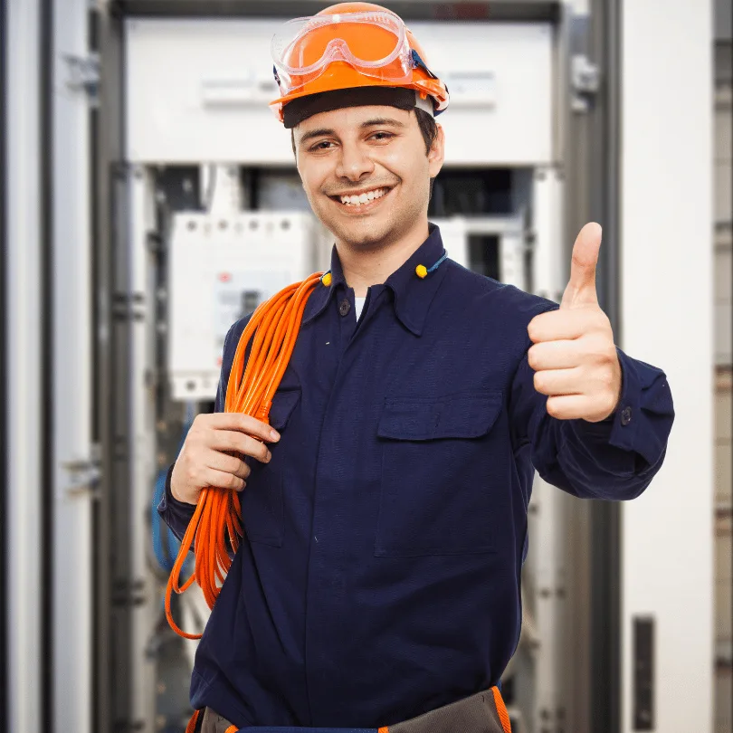 Junger Elektroinstallateur in Arbeitsuniform mit orange Schutzhelm, Schutzbrille und Stromkabel, Daumen hoch